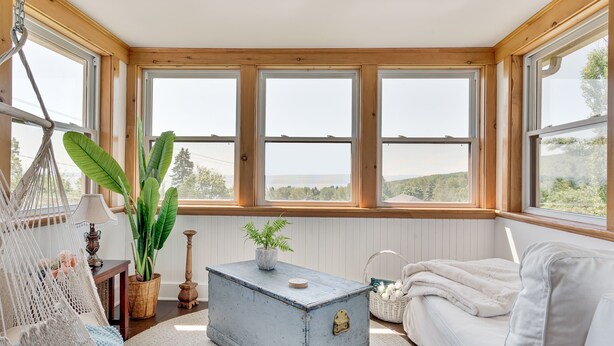 A cozy room with a hammock, a white sofa, a wooden chest, and large windows overlooking a scenic view. - Ancestral home, Charlevoix - Saint-Irénée Beach & St. Lawrence River view (Saint-Irénée)