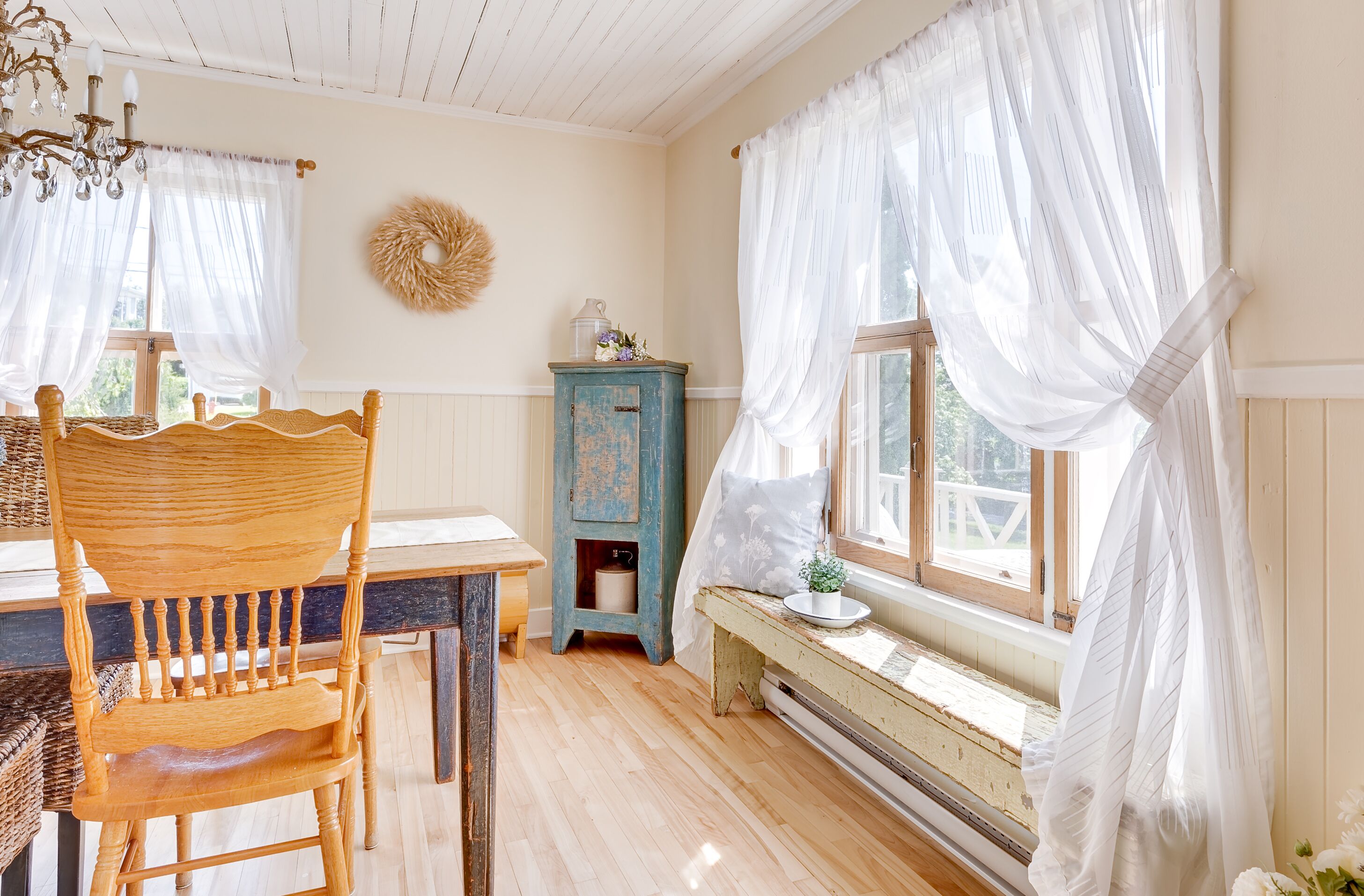 Ein Zimmer mit einem Holzbett, einem Tisch, einem blauen Schrank und durchsichtigen Vorhängen.