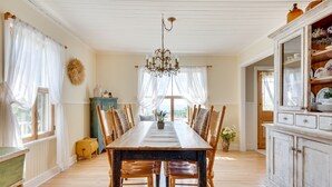A dining room with a long wooden table, surrounded by chairs, a chandelier, and a cabinet with dishes. - Ancestral home, Charlevoix - Saint-Irénée Beach & St. Lawrence River view (Saint-Irénée)