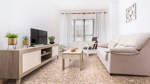 Ein Wohnzimmer mit Fernseher, Sofa, Couchtisch und Pflanzen.