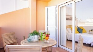 A small balcony with a round wooden table, two chairs, and a fruit bowl. A sliding glass door leads to a bedroom with a bed and a nightstand. - Home2Book Stunning Apartment Candelaria, Terrace (Las Caletillas)