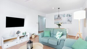 A modern living room with a sofa, a TV, a ceiling fan, and a wall-mounted artwork. - Home2Book Stunning Apartment Candelaria, Terrace (Las Caletillas)