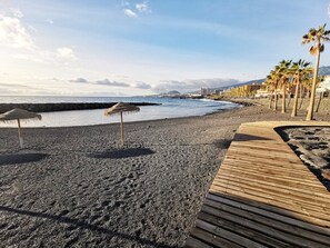 Ein Strand mit einer Holzpromenade, Palmen und einer felsigen Küstenlinie.