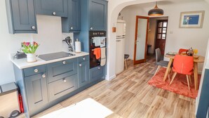 A compact kitchen with blue cabinets, a sink, and a stove. There's a dining area with a table and chairs, and a hallway leading to another room. - Robellen Corner (Banbury)