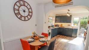 A modern kitchen with dark cabinets, a wooden dining table with red chairs, and a large wall clock. - Robellen Corner (Banbury)