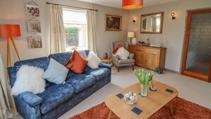 A living room with a blue sofa, a wooden coffee table, and a red rug. - Robellen Corner (Banbury)