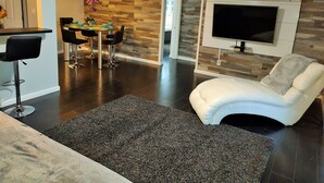 A modern living room with a dark wood floor, a white leather sofa, a dining area with a round table and black chairs, and a mounted TV. - Beautiful Waterfront apartment 2 bdrm: sand, Beach (Treasure Island)