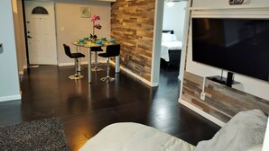 A modern living room with a flat-screen TV, dark hardwood flooring, a white sofa, and a dining area with a glass table and black chairs. - Beautiful Waterfront apartment 2 bdrm: sand, Beach (Treasure Island)