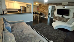 A modern living room with a sofa, a coffee table, and a TV mounted on the wall. There is a kitchen area with cabinets and a refrigerator. - Beautiful Waterfront apartment 2 bdrm: sand, Beach (Treasure Island)