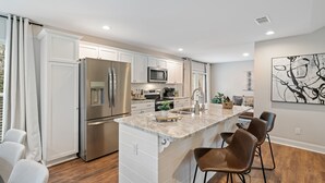 A modern kitchen with white cabinetry, stainless steel appliances, a marble island, and bar stools. - Hamilton Hideaway- Pool, Creek View w/ Scenic Deck (Mobile)