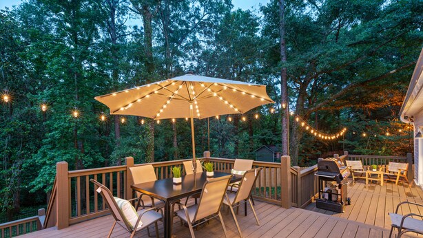 A wooden deck with a table and chairs, surrounded by trees and string lights. - Hamilton Hideaway- Pool, Creek View w/ Scenic Deck (Mobile)