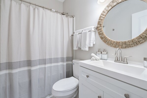 A bathroom with a shower curtain, a toilet, a sink with a mirror, and a towel rack. - Hamilton Hideaway- Pool, Creek View w/ Scenic Deck (Mobile)