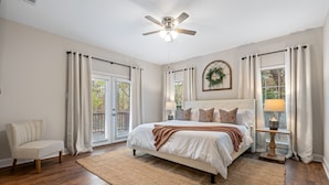 A bedroom with a bed, a chair, a rug, a ceiling fan, and a window with curtains. - Hamilton Hideaway- Pool, Creek View w/ Scenic Deck (Mobile)
