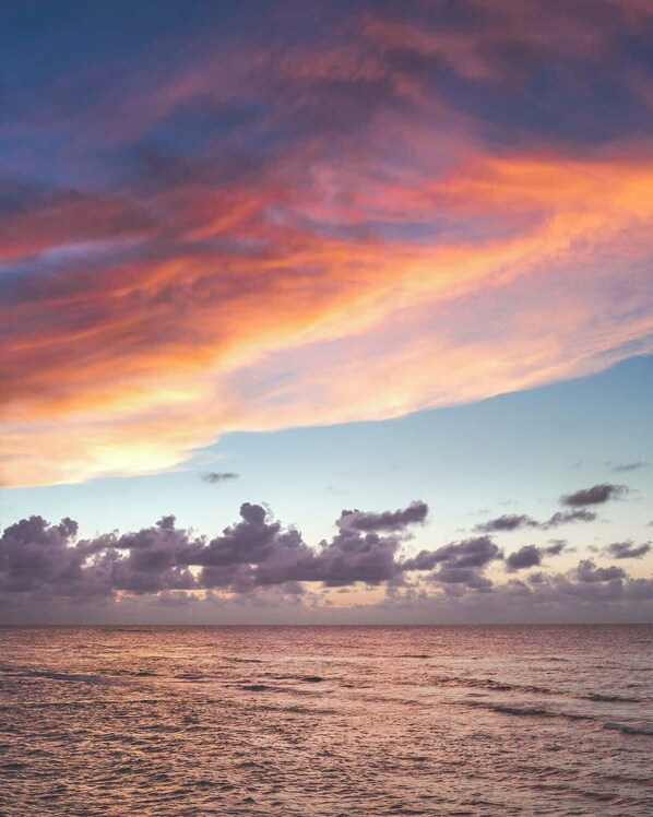 Una puesta de sol sobre un mar tranquilo con horizonte despejado y nubes dispersas.