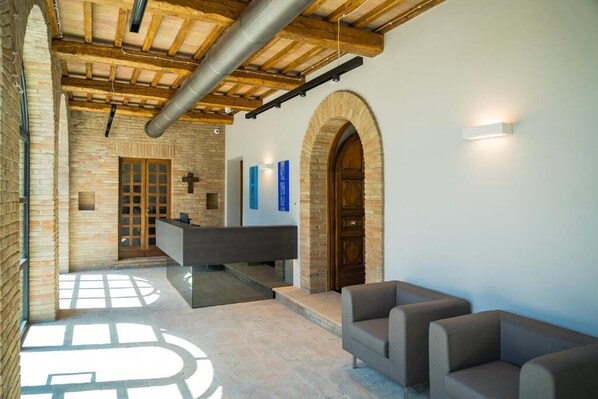 A reception area with a reception desk, two sofas, and a cross on the wall. - Le Cappuccinelle Suites&SPA (Perugia)