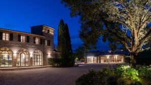 A large, well-lit brick building with arched windows and a prominent tower, surrounded by trees and a driveway. - Le Cappuccinelle Suites&SPA (Perugia)