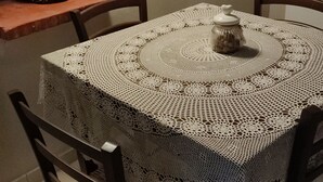 A dining table with a crocheted tablecloth, surrounded by wooden chairs. A basket is placed on a brick ledge above the table. - Casedda Ostunese (Ostuni)