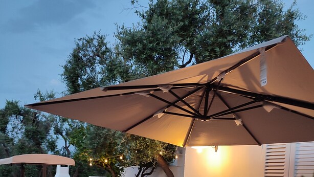 An outdoor patio with a table and chairs, a pizza oven, and string lights. - Casedda Ostunese (Ostuni)