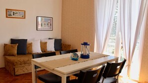 Een kamer met een bank, een tafel, stoelen, een lamp en twee foto's in lijsten aan de muur.