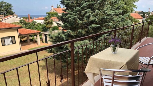 Ein Balkon mit Tisch und Stühlen, mit Blick auf eine Wohngegend mit Häusern und einem Baum.
