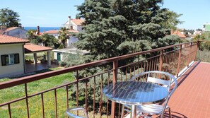 Un balcon avec une balustrade en métal, une table ronde en verre et des chaises.