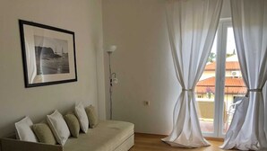 Ein Wohnzimmer mit einer Couch, einem gerahmten Bild und einem Fenster mit Vorhängen.