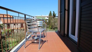 Ein Balkon mit einem Metallstuhl, gefliestem Boden und Blick auf angrenzende Gebäude.