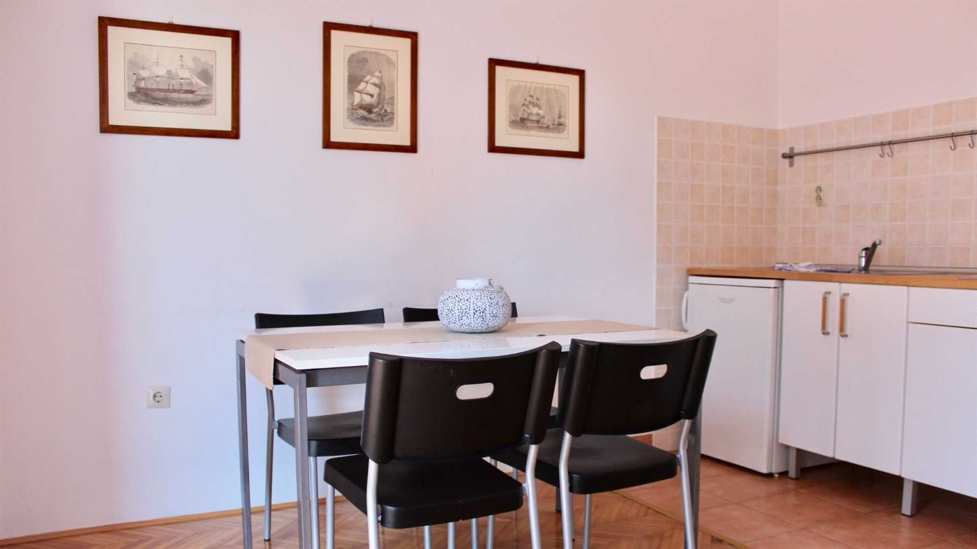 A small dining area with a table and chairs, a white cabinet, and a tiled backsplash in the kitchen.
