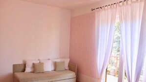 Ein Zimmer mit einem beigefarbenen Sofa, weißen Kissen und einem Fenster mit durchsichtigen Vorhängen.
