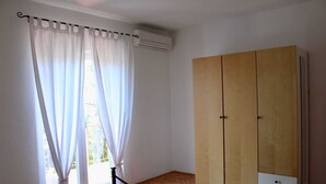 Ein Zimmer mit großem Fenster, das mit durchsichtigen Vorhängen versehen ist, einem Holzschrank und einer Klimaanlage an der Wand.