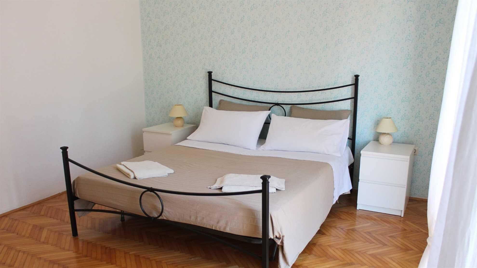 Un lit bien fait, avec un cadre en métal, deux tables de chevet avec des lampes et un papier peint à motifs.