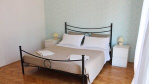 Ein ordentlich bezogenes Bett mit Metallgestell, zwei Nachttische mit Lampen und rahmigem Wandpapier.