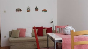 Una stanza piccola e accogliente con un divano, un tavolo e una sedia. Sopra il divano sono presenti tre elementi decorativi a parete.