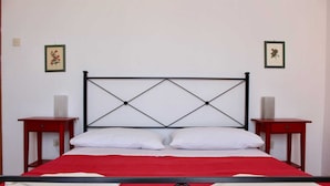 Un letto con copriletto rosso, una testiera in metallo nero e due comodini con lampade.