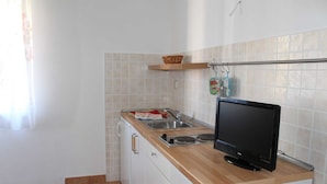 Una cucina compatta con un piano di lavoro in legno, un lavandino in acciaio inossidabile e una TV a schermo piatto nera.
