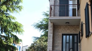 Un edificio a due piani con facciata in pietra, un balcone con ringhiere in metallo e una porta con finestra.