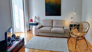 A living room with a beige sofa, a wicker chair, a white rug, and a painting on the wall. - Dear Home ★ In the Heart of Lisbon (Lisboa)