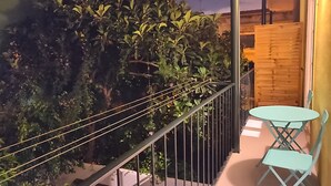 A balcony with a metal railing, a small table, and two chairs. There is dense foliage in the background. - Dear Home ★ In the Heart of Lisbon (Lisboa)