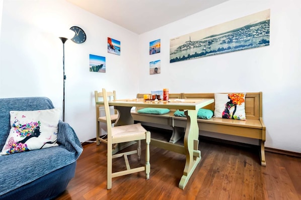 A cozy room with a wooden dining table, a sofa, and a bench. There are several paintings on the walls and a clock.