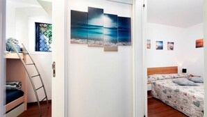 A bedroom with a bunk bed, a wooden ladder, a bed with a floral-patterned duvet, and a wall with three framed artworks depicting a beach scene. - HAVANA - Apartment with Sea View (Rovinj)