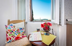 A cozy corner with a chair, a table, a book, a mug, and a vase with flowers.