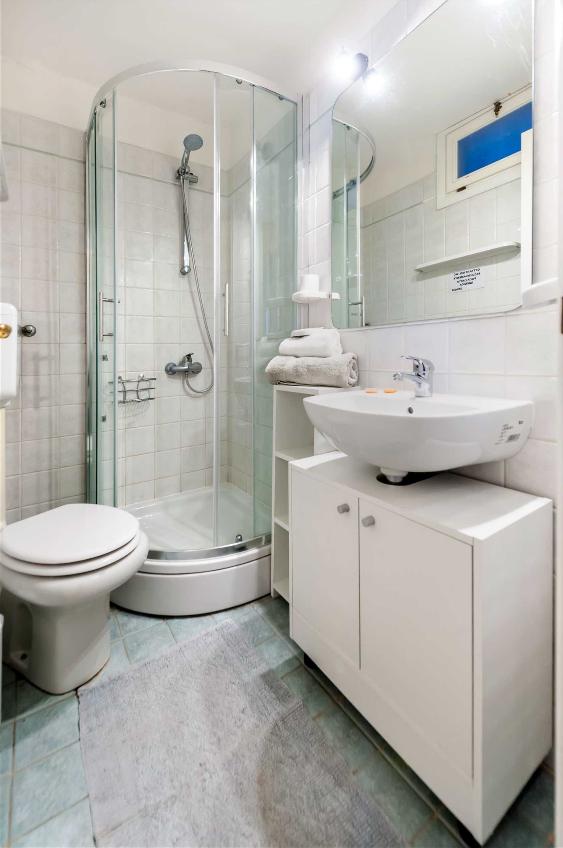 Et moderne badeværelse med et glasafskærmet brusebad, en hvid vask og et toilet.
