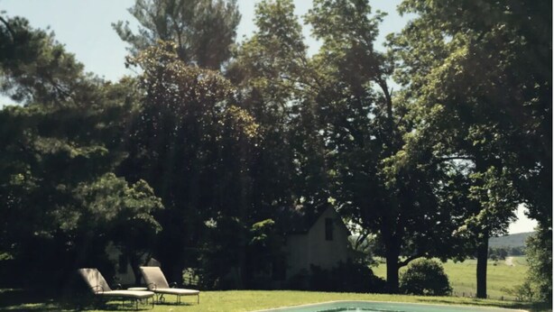 Ein rechteckiger Pool mit einer Rasenfläche davor, umgeben von Bäumen und einem Haus im Hintergrund.