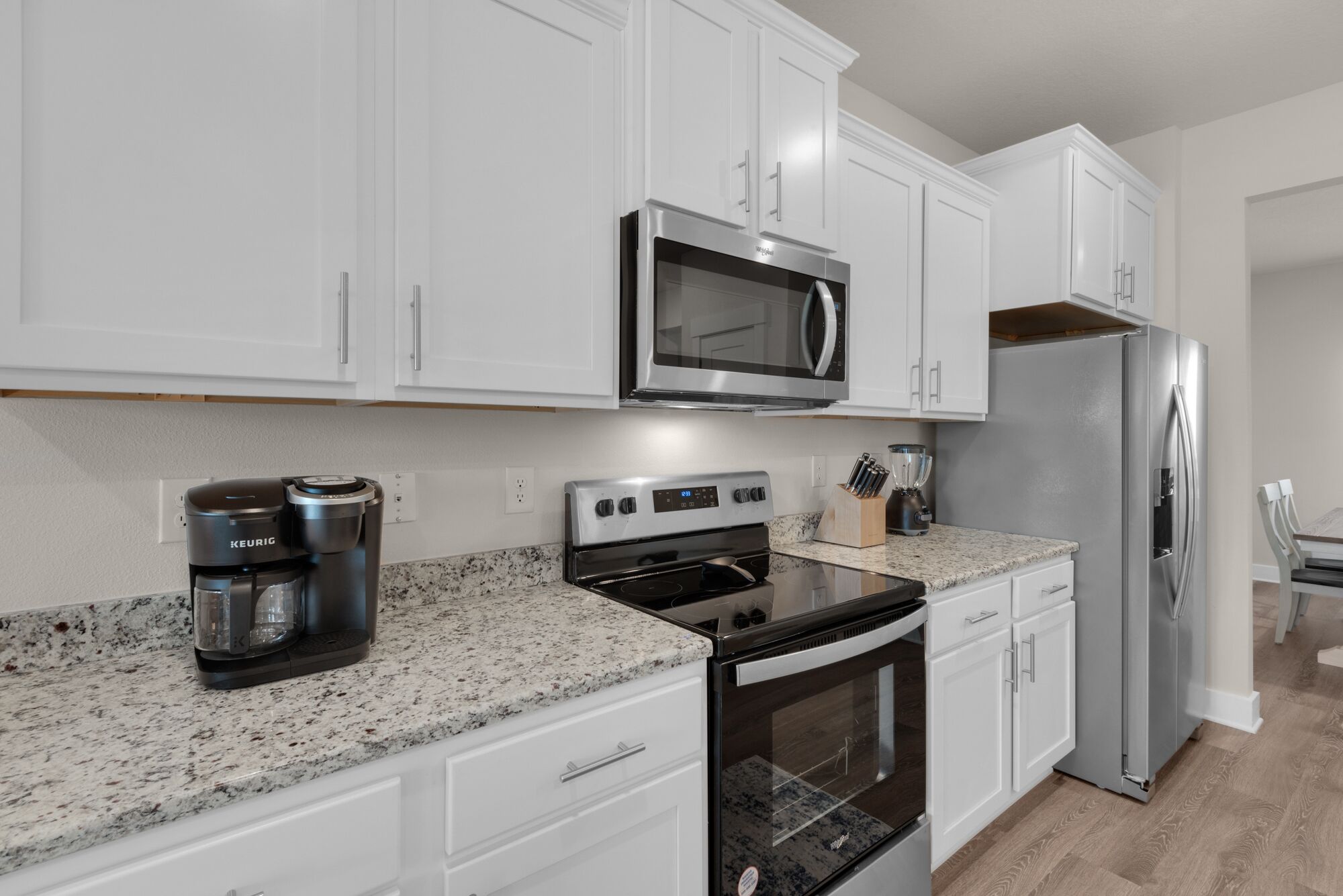 A modern kitchen with white cabinets, a stainless steel microwave, a built-in oven, and a refrigerator.