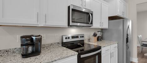 A modern kitchen with white cabinets, a stainless steel microwave, a built-in oven, and a refrigerator.