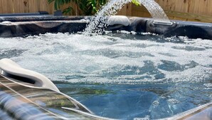 A hot tub with a waterfall feature, surrounded by a wooden fence and greenery.