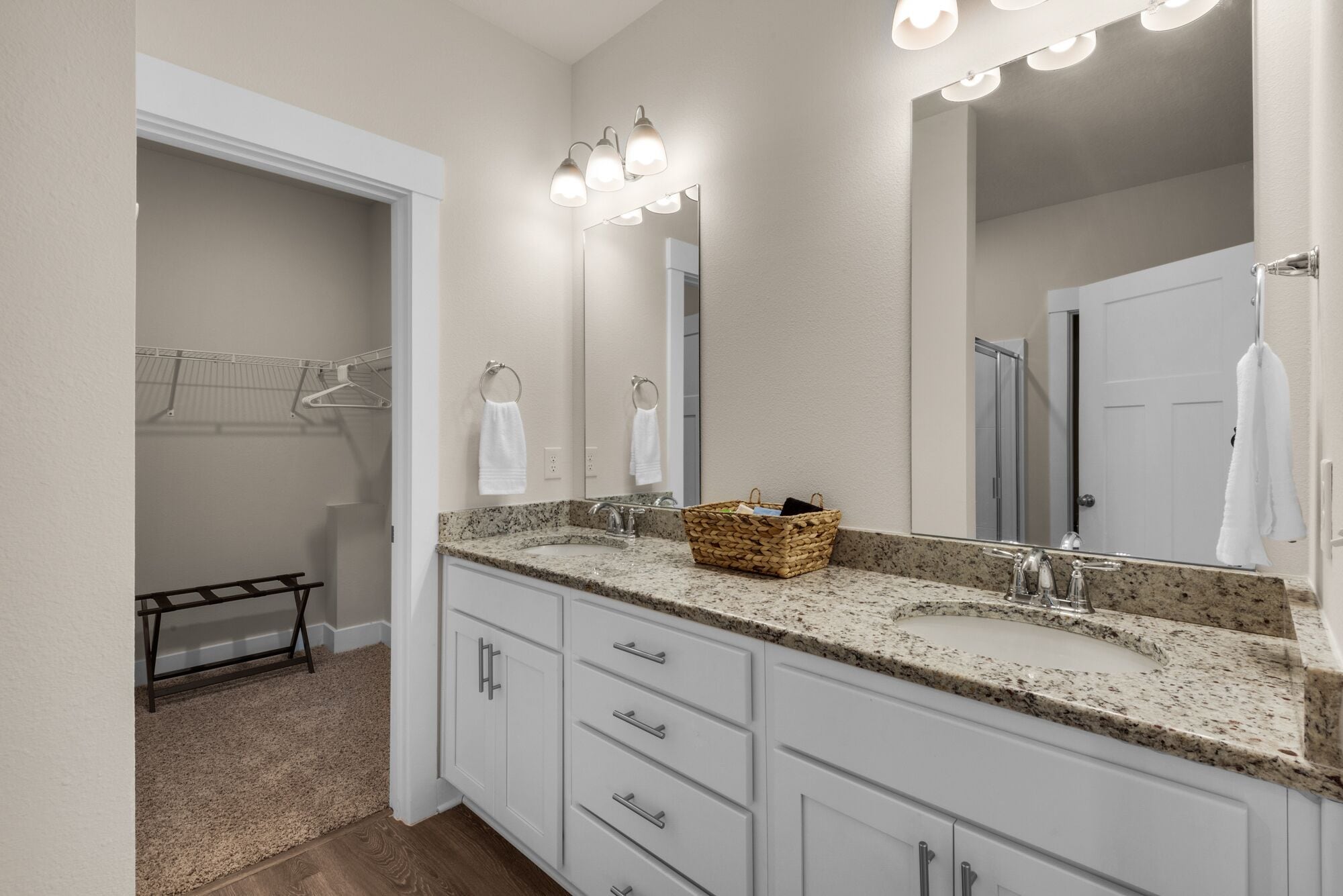 A modern bathroom with two sinks, a large mirror, and a basket on the countertop.