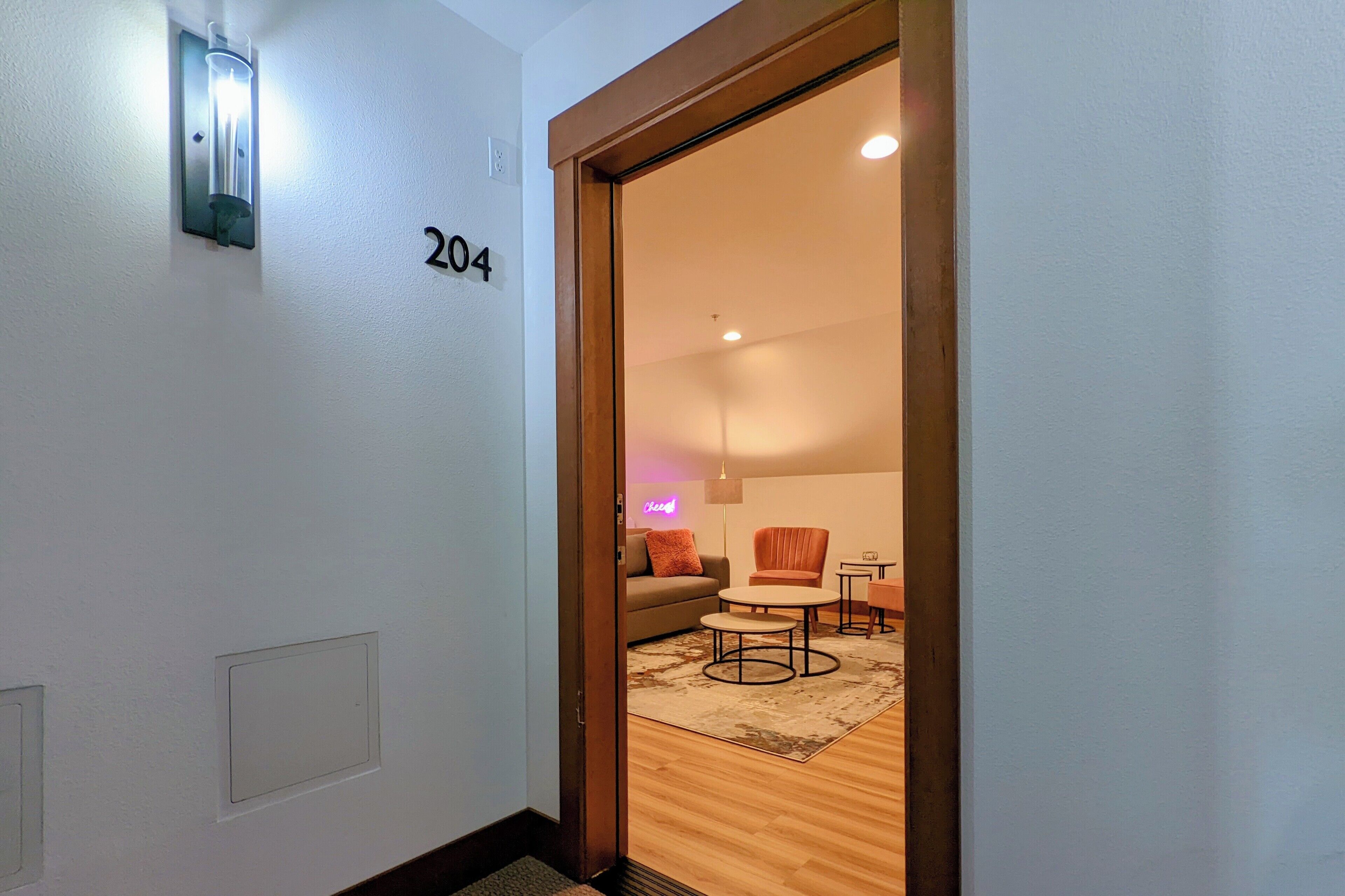 A hallway with a door marked '204' leading to a living area with a sofa, armchair, coffee table, and a small table.