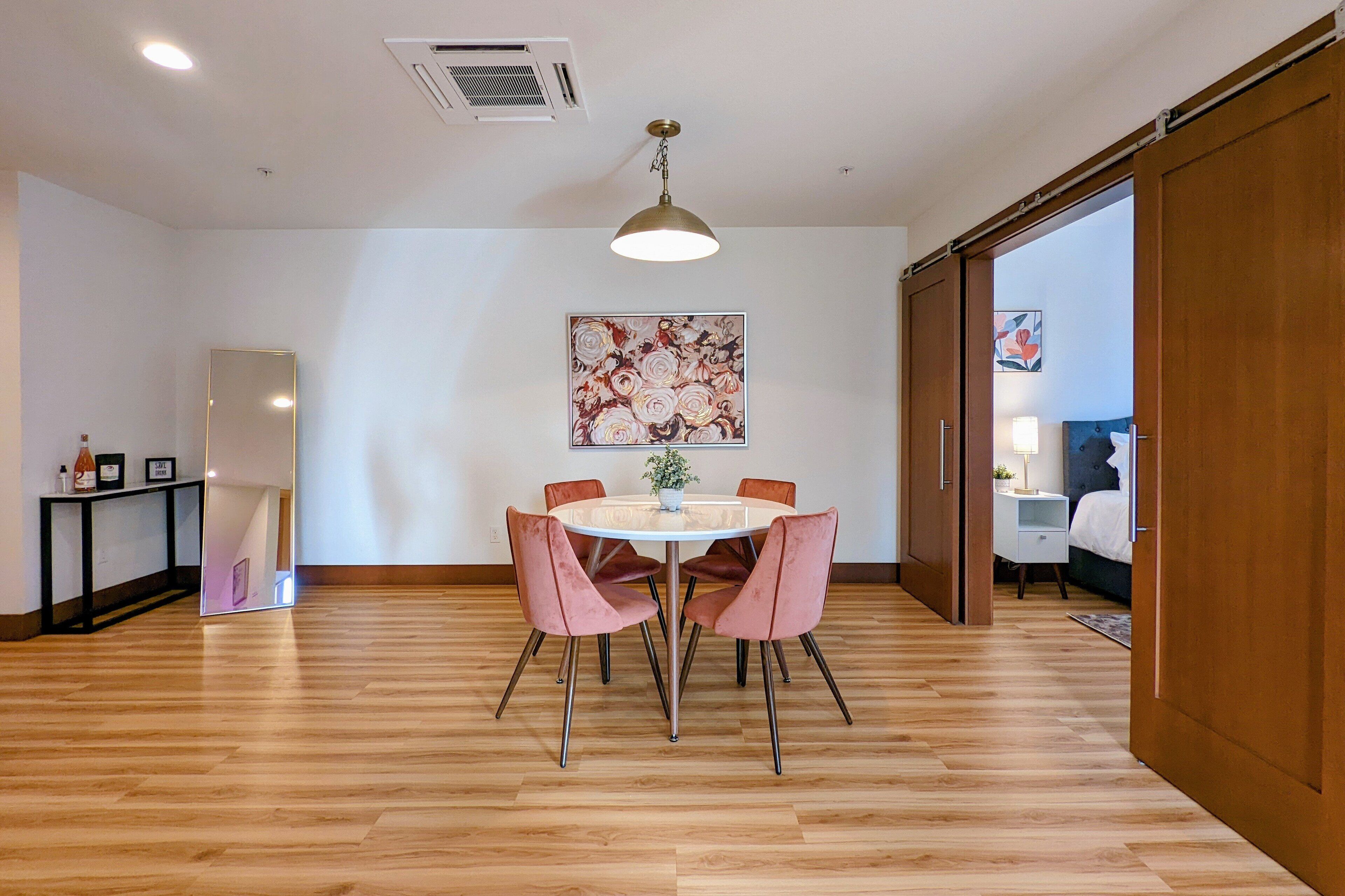 Un coin repas comprenant une table ronde, quatre chaises, un luminaire suspendu et un tableau floral accroché au mur.