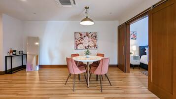 Un coin repas comprenant une table ronde, quatre chaises, un luminaire suspendu et un tableau floral accroché au mur.